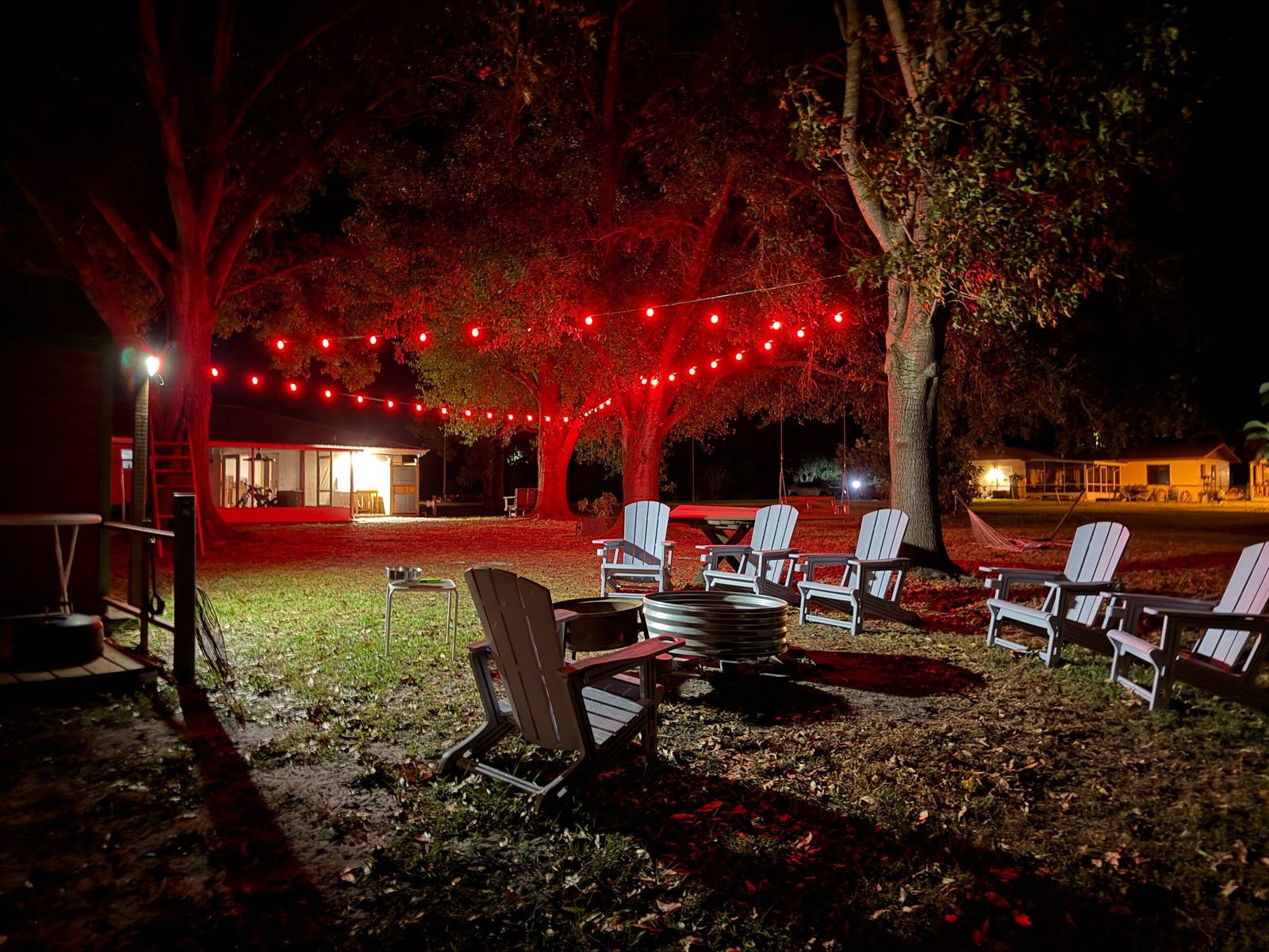 Fire pit circle with Adirondack chairs under red string lights at night