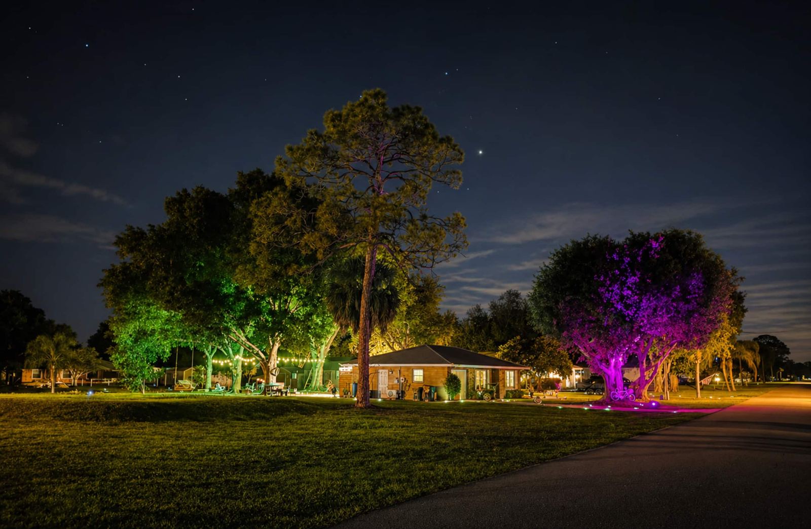 Night view of the property with colorful landscape uplighting in the oak trees