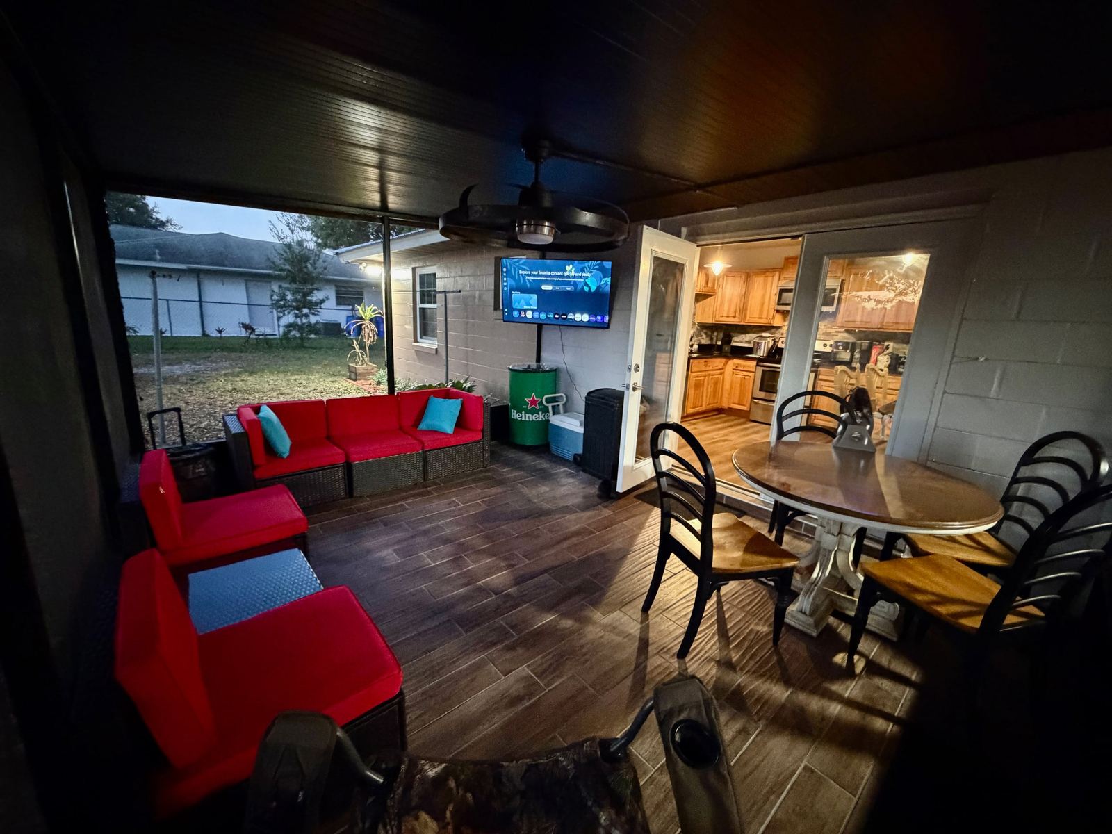 Screened patio at dusk with outdoor smart TV, dining table, and beverage cooler